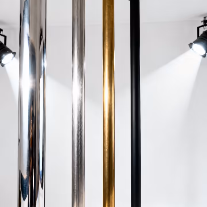 A lineup of four different dance poles showing various finishes: shiny chrome, matte stainless steel, golden brass, and black powder coat.