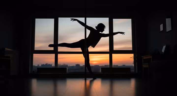 A person dancing freely and expressively on their home pole, silhouetted against a sunset window, representing privacy and personal joy.